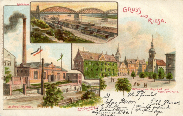 Alte Postkarte zeigt Stadtansicht mit Gebäuden, Bäumen, Strommasten, Flaggen, Brücke, rauchendem Zug auf Schienen und Himmel, mit handschriftlichem Text auf der Vorderseite.