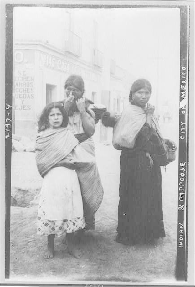 Drei Frauen, die nebeneinander auf einer Straße in Mexiko-Stadt stehen, mit Gebäuden im Hintergrund, auf einem Schwarz-Weiß-Foto.