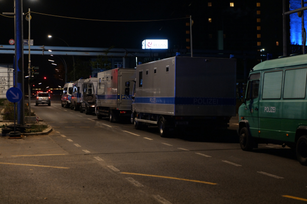 Lange Reihe von Lastwagen, die nachts am Straßenrand geparkt sind, mit Fahrzeugen, Straßenlaternen, Schildern und Gebäuden im Hintergrund.