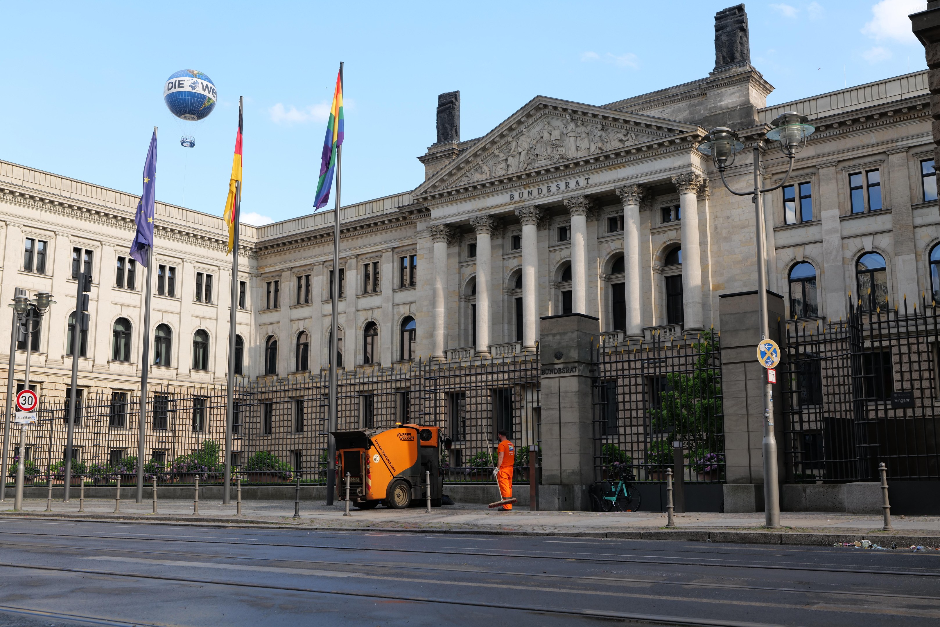 Large modern government building with many windows, surrounded by street infrastructure, pedestrians, and trees, with a cloudy sky in the background; identified as the Bundestag in Berlin, Germany.