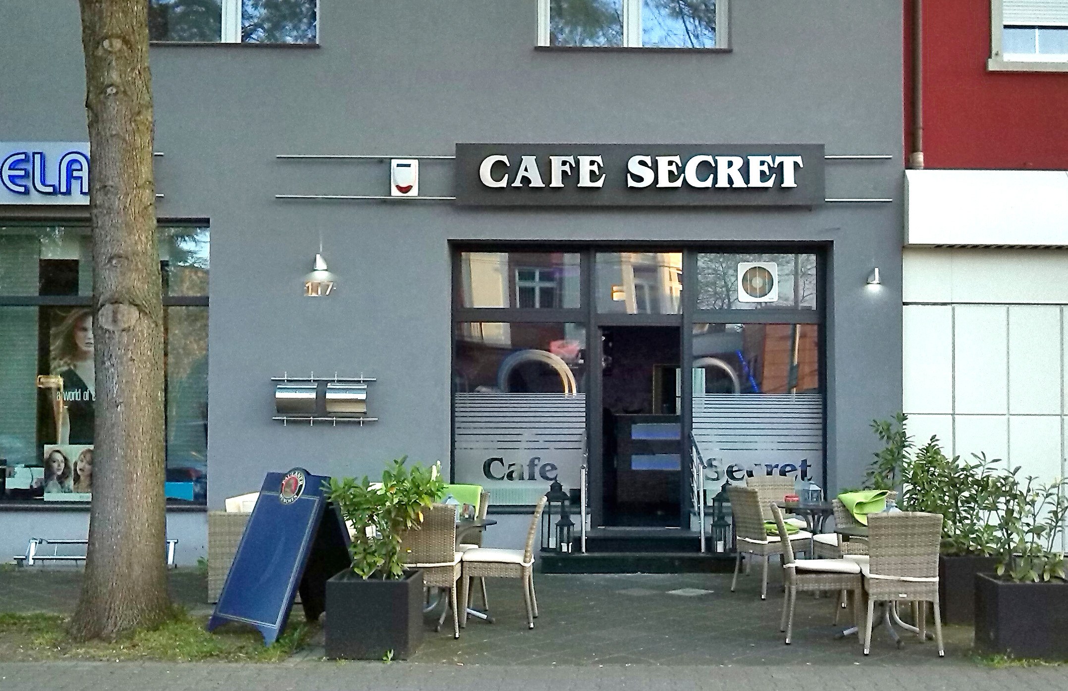Cafe Secret in Berlin, Germany, with outdoor seating, potted plants, a signboard, and a tree.