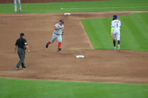 Ein Baseballspieler in einem Sportsitzug läuft Richtung erste Base, mit zwei anderen Spielern im Hintergrund.