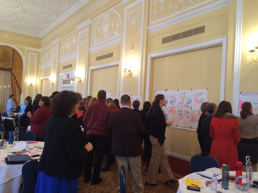 Eine Gruppe von Menschen untersucht Plakate und Diagramme, die an einer Wand in einem Kunstmuseum zu sehen sind.