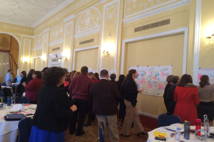 Eine Gruppe von Menschen untersucht Plakate und Diagramme, die an einer Wand in einem Kunstmuseum zu sehen sind.