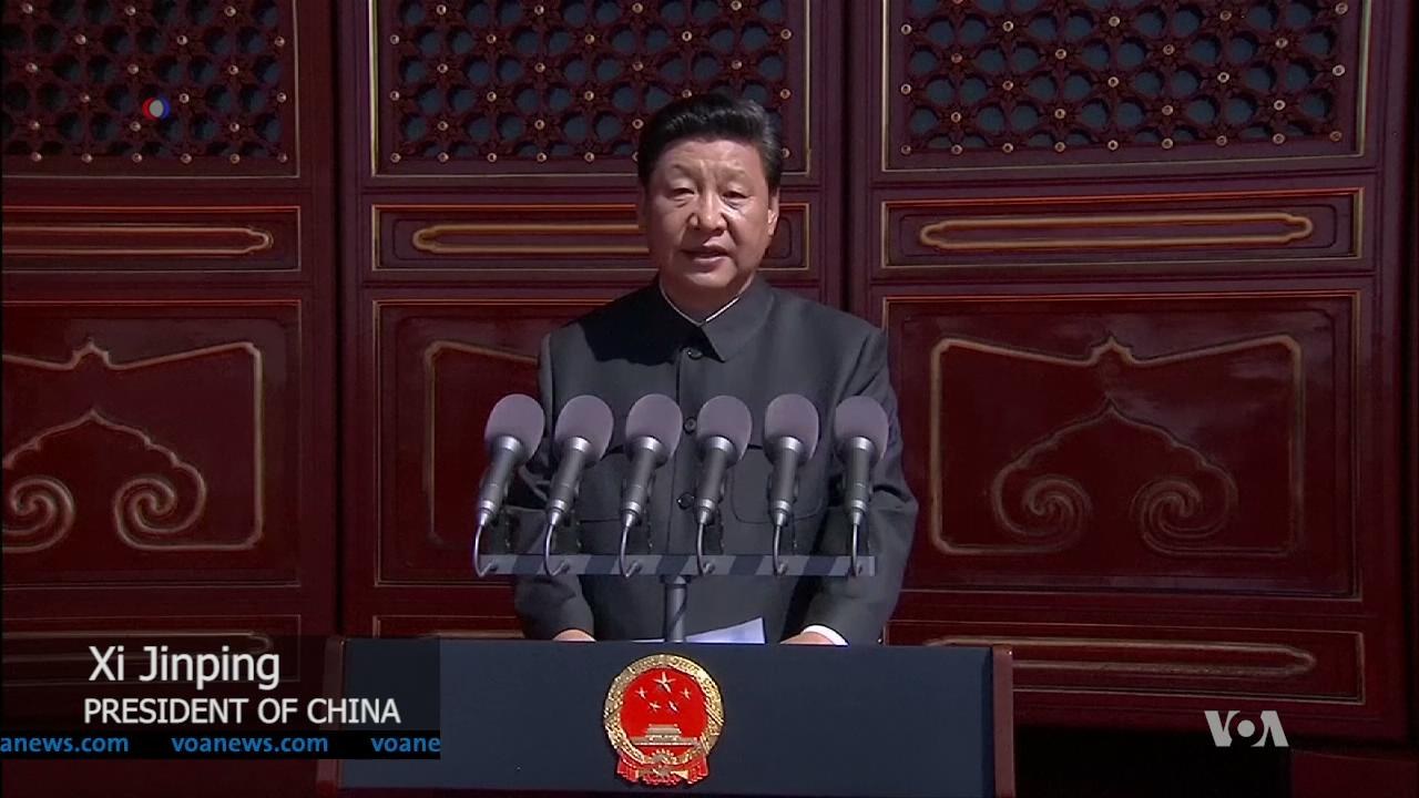 Xi Jinping steht an einem Podium mit Mikrofonen und einem Logo, während er eine Rede in der Großen Halle des Volkes in Peking hält, mit einer hölzernen Wand im Hintergrund.