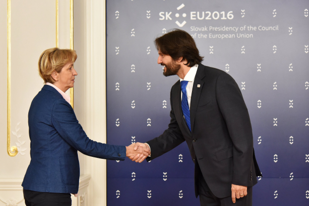 Bundeskanzlerin Angela Merkel und Bundeskanzler Joachim Gauck schütteln sich vor einer Wand mit einem 'EU-Gipfel'-Banner und einer Tür im Hintergrund die Hände, beide lächeln.