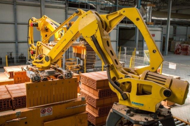 Großes Industriegebäude mit gestapelten Kisten, Kranen, Zaun, Pfählen und einer fernen Wand in einer automatisierten Fertigungsumgebung.