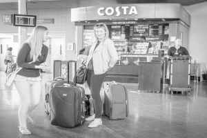 Zwei Frauen mit Gepäck vor einem Coffeeshop, wahrscheinlich am Flughafen.