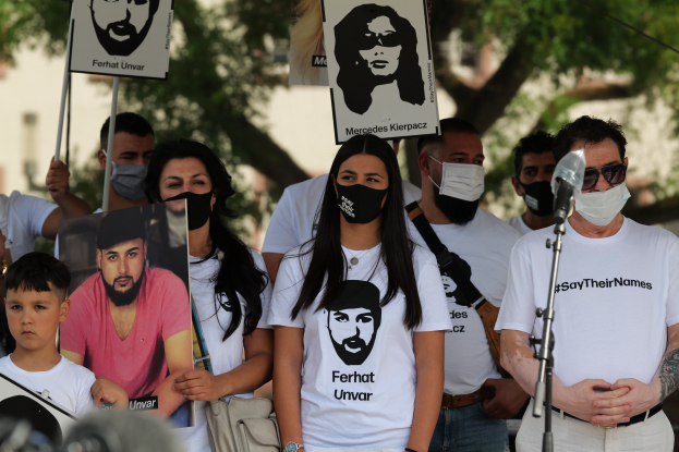Eine Gruppe von Menschen mit Masken hält Schilder vor einer Menge auf einer Demonstration in Mexiko-Stadt, mit einem Mikrofon und einer Kamera im Vordergrund.