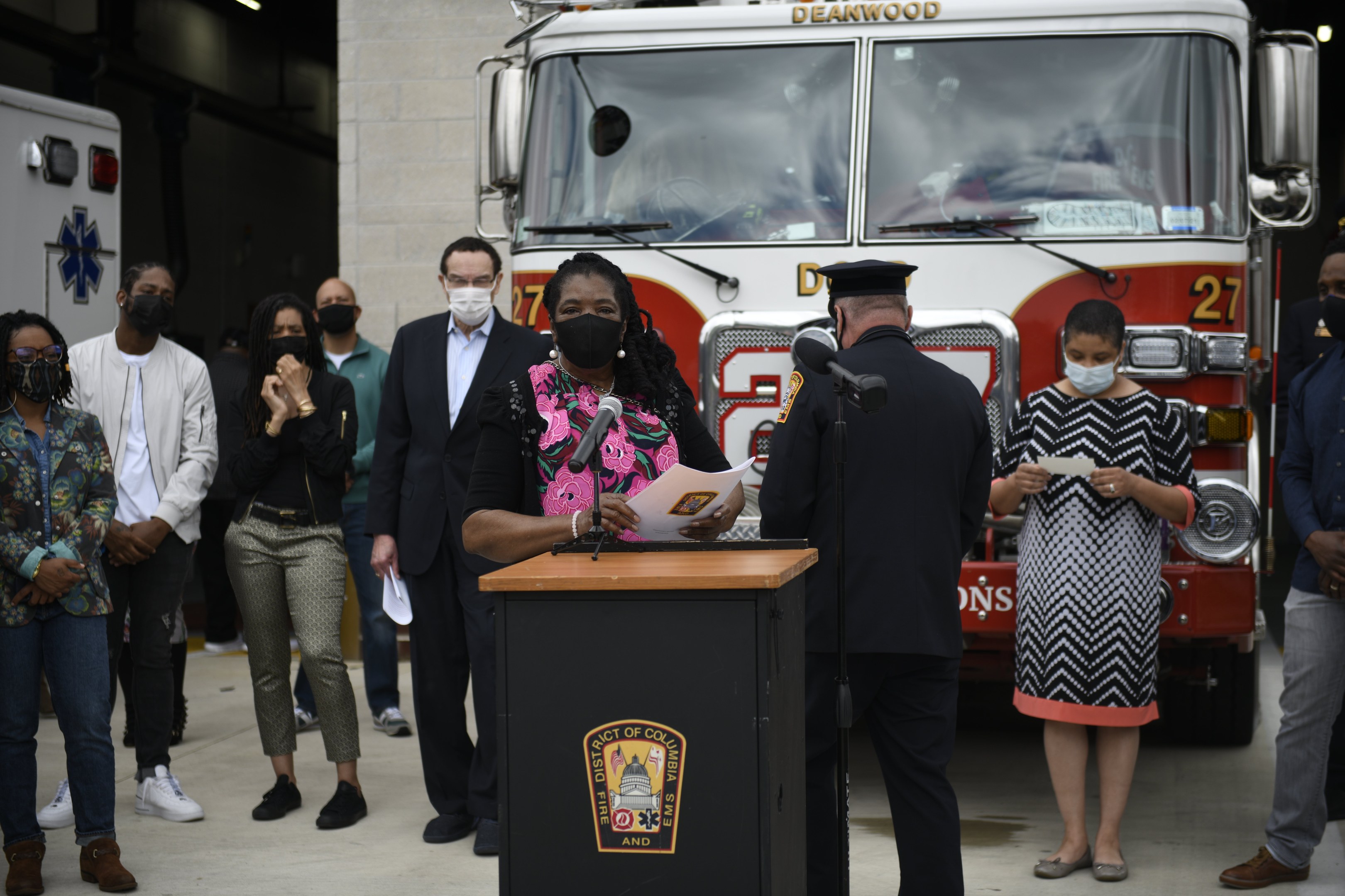 Bürgermeisterin Lori Lightfoot spricht auf einer Pressekonferenz vor einem Feuerwehrauto, mit einer Gruppe maskierter Personen, Mikrofonen auf Podesten, Papieren und einer beleuchteten Wand im Hintergrund.