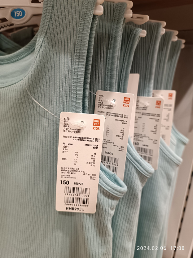 Eine Reihe blauer T-Shirts für Kinder hängt an einem Ladengestell, jedes mit einem Preisschild beschriftet "Uniqlo Kids."