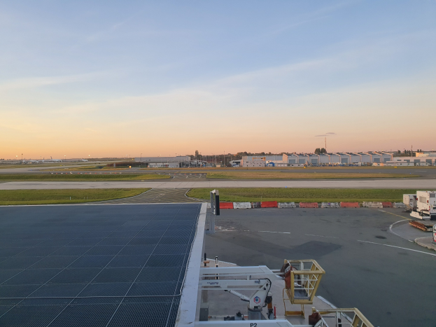 Luftbild eines Flughafens mit Fahrzeugen auf der Straße, Grünflächen, Gebäuden, Bäumen und einem bewölkten Himmel, mit einer Solarzelle auf dem Dach eines Gebäudes.