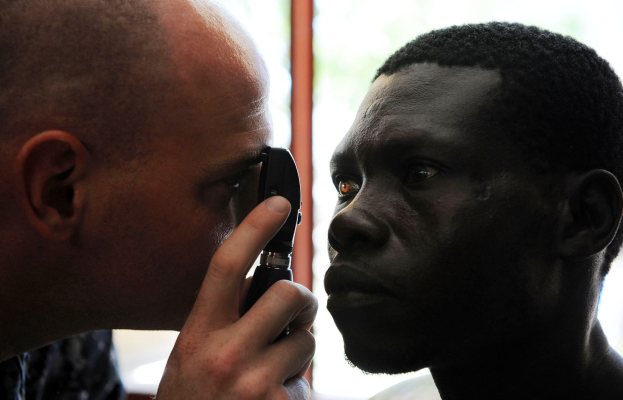 Ein Mann bei einer Augenuntersuchung durch einen Arzt, der ein ophthalmisches Instrument hält.