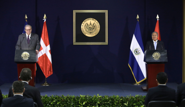 Zwei Männer stehen an Rednerpulten und sprechen vor einem sitzenden Publikum, wobei der Mann links als Juan Manuel Santos, Präsident von Chile, identifiziert wird.