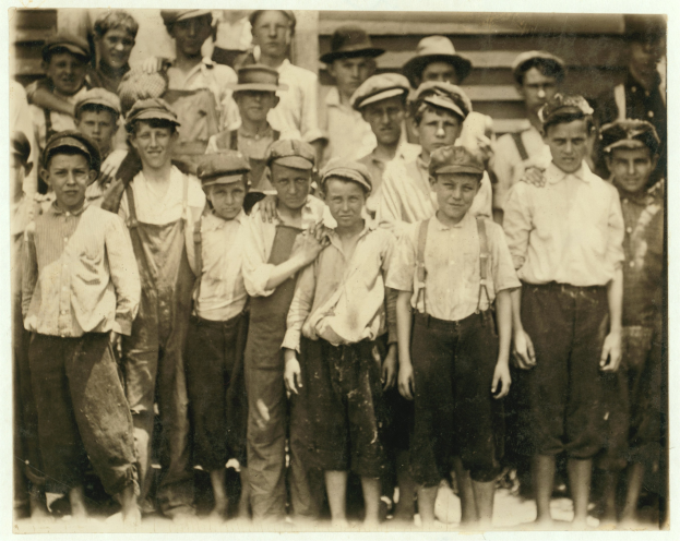 Schwarzes und weißes Foto einer Gruppe von jungen Jungs mit Mützen, die in einer Reihe vor einem Geb├Ąude stehen.
