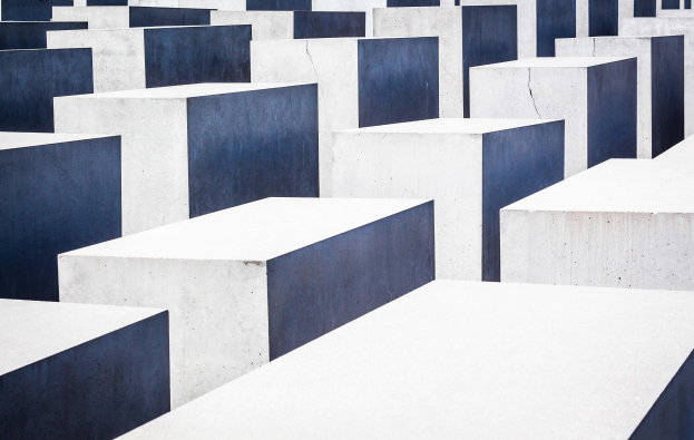Luftaufnahme des Holocaust-Mahnmals für die ermordeten Juden Europas in Berlin, das aus zahlreichen weißen und blauen rechteckigen Betonsteinen besteht, die in einem Gittermuster angeordnet sind.