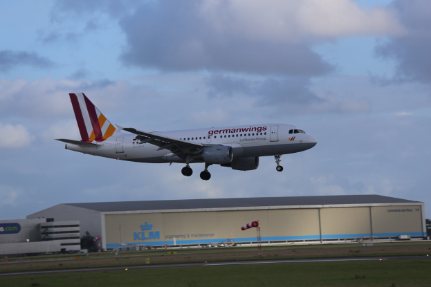 Germanwings Airbus A320-200 beim Abheben vom Frankfurter Flughafen mit Gras darunter, einem Gebäude im Hintergrund und Wolken am Himmel.