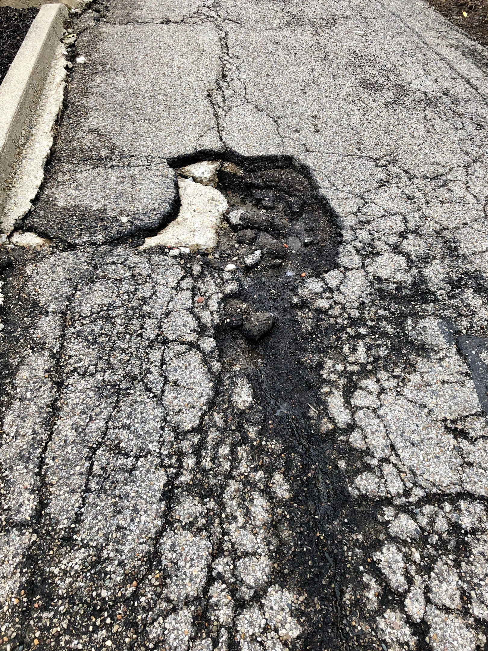 Eine Straße mit einem großen Schlagloch in der Mitte, umgeben von kleinen Steinen und einer Wand auf der linken Seite.