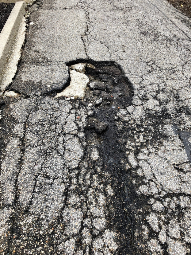 Eine Straße mit einem großen Schlagloch in der Mitte, umgeben von kleinen Steinen und einer Wand auf der linken Seite.
