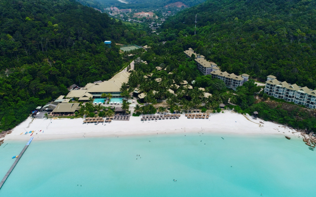 Luftaufnahme eines Strandresorts in Koh Samui, Thailand, mit einer Brücke auf der linken Seite, Gebäuden, Bäumen, Hügeln und einigen Menschen am Strand.