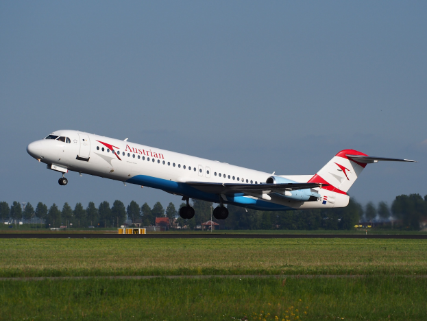 Austrian Airlines Embraer ERJ-190 Flugzeug beim Start vom Frankfurt Airport, mit grünem Gras darunter und Bäumen und Gebäuden im Hintergrund unter einem sichtbaren Himmel.