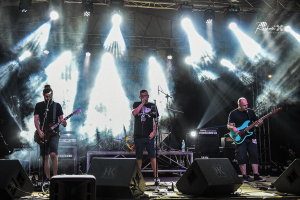 Drei M├Ąnner auf der B├╝hne, die Gitarren spielen und in Mikrofone singen, umgeben von Musikausr├╝stung und einem Banner mit Text und Lichtern im Hintergrund beim Belgrade Music Festival in Serbien im Jahr 2016.