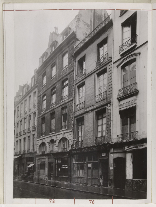 Schwarzes und wei├čes Foto einer Stra├če mit Geb├Ąuden, Fenstern, Gel├Ąndern, Namensschildern und einer Stra├če unten.