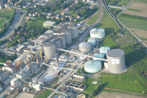 Luftaufnahme mit mehreren Gebäuden, Häusern, Bäumen und Fahrzeugen auf einer Straße, umgeben von Gras.