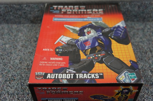 Ein roter, oranger und blauer Autobot Tracks Roboterkasten mit schwarzem unscharfen Hintergrund.