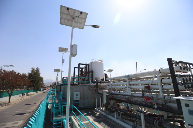 Großes industrielles Gebäude mit ausgedehnten Rohrleitungen und Solarpanelen auf dem Dach, vor den Hügeln und einem klaren blauen Himmel, Teil der neuen Wasseraufbereitungsanlage von Kalifornien.