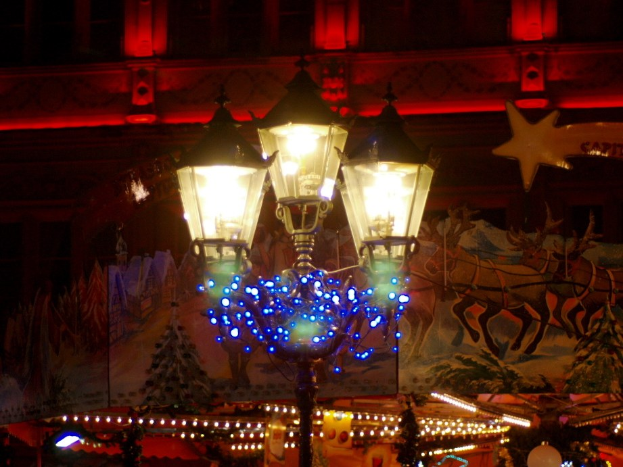 Eine festlich geschmückte Straßenlaterne mit Lichtern steht in einer Stadt bei Nacht, mit einem Gebäude im Hintergrund.