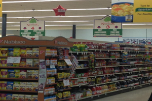 Ein Supermarkt-Innenraum mit sichtbaren Lebensmitteln, Deckenbeleuchtung und Beschilderung.