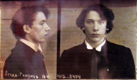 Schwarz-weiß-Foto eines Mannes in schwarzem Anzug, weißem Hemd und schwarzer Krawatte mit zurückgekämmtem Haar, verschränkten Händen, strenger Miene und Text, der seine Verbrechen beschreibt.