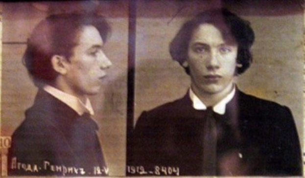 Schwarz-weiß-Foto eines Mannes in schwarzem Anzug, weißem Hemd und schwarzer Krawatte mit zurückgekämmtem Haar, verschränkten Händen, strenger Miene und Text, der seine Verbrechen beschreibt.
