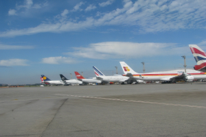 Mehrere Flugzeuge sind auf einer Rollbahn mit Polen und Kabeln in der Nähe, unter einem bewölkten Himmel.