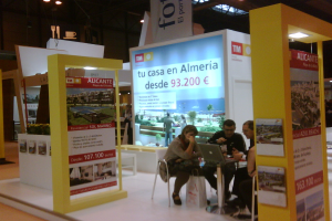 Eine Gruppe von Menschen sitzt um einen Tisch herum auf Stühlen und schaut auf einen Laptop, mit mehreren Flyern, auf denen verschiedene Werbeanzeigen zu sehen sind.