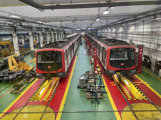 Zwei Züge auf den Gleisen in einer großen Industriehalle mit Maschinen, Rohren und Deckenbeleuchtung, Teil der neuen Zugproduktion der Daimler AG.