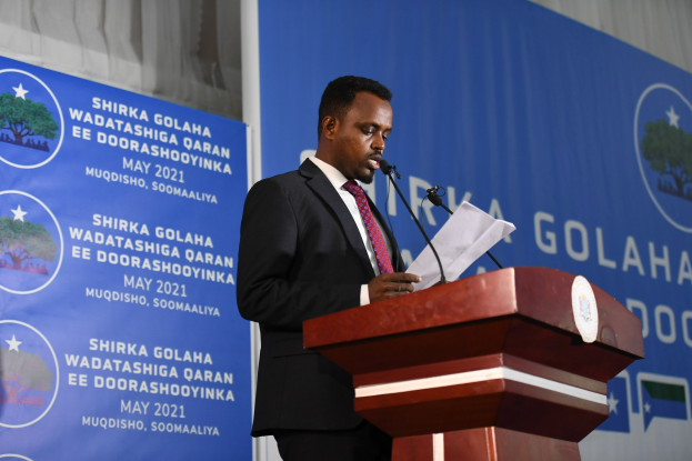 Ein Mann im Anzug spricht an einem Podium mit Papieren, einem Banner und Vorhängen hinter ihm, wahrscheinlich zur Ankündigung der neuen Regierung Ghanas.