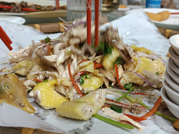 A table with plates of food, bowls of sauce, chopsticks, glasses, bottles, and other objects in a restaurant or bar setting, with a person visible in the background.