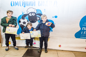 Drei Kinder halten Papiere in den Händen und stehen vor einem Banner.