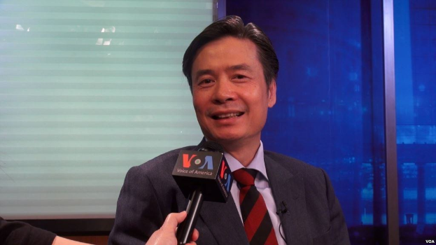 Ein Mann in Anzug und Krawatte hält ein Mikrofon, während eine Reporterhand links zu sehen ist, während er in der Nähe eines Fensters interviewt wird.