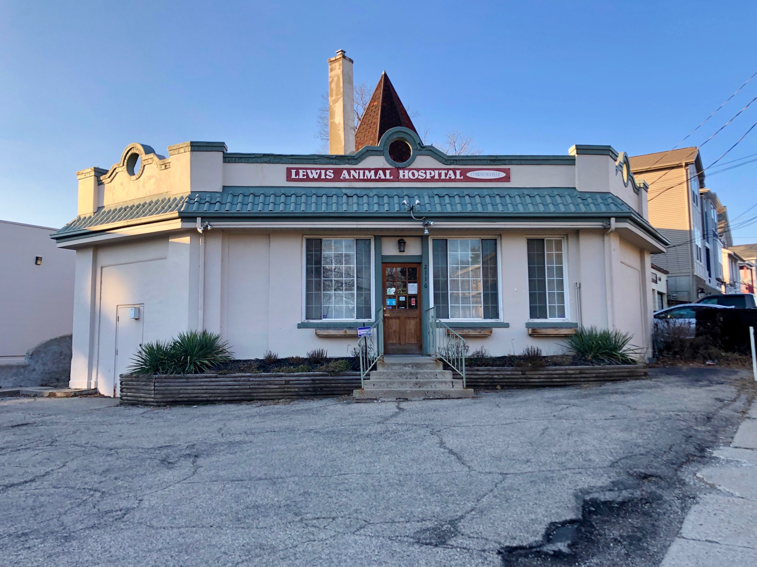 Außenansicht der Lewis Animal Hospital in San Francisco, ein Gebäude mit Fenstern und einer Tür, umgeben von Pflanzen und Treppen mit Geländern, mit einem Schild an einem Pfahl, parkenden Fahrzeugen in der Nähe, sichtbarem Himmel und Überlandleitungen.