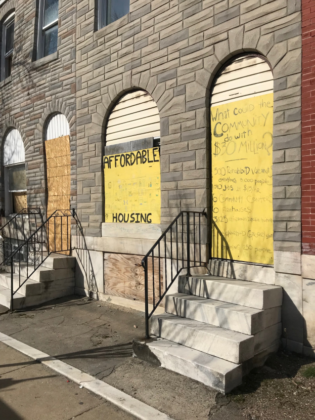 Verschlossenes Gebäude mit "Bezahlbarer Wohnungen"-Schild, Treppe mit Geländer und Straße unten.