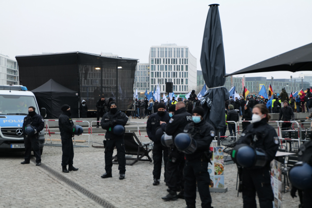 Polizeibeamte in Einsatzausrüstung stehen hinter Barrieren einer Menge von Demonstranten mit Helmen und Masken während einer Demonstration in Berlin gegen Regierungskürzungen.