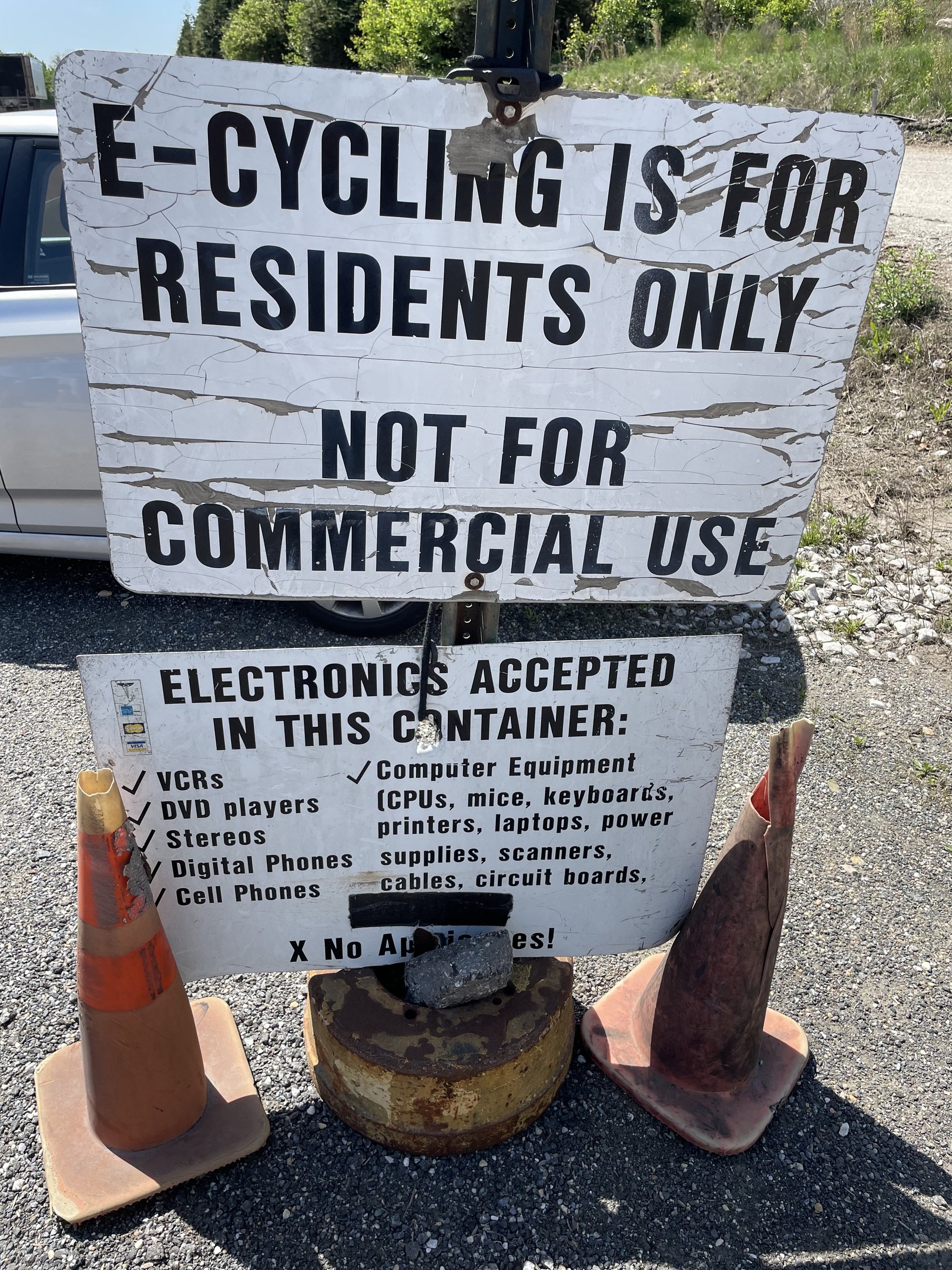 Schild mit der Aufschrift "E-Bike-Fahren nur für Anwohner" neben einer Straße mit Verkehrskegeln, einem Fahrzeug, Bäumen und einem klaren blauen Himmel im Hintergrund.