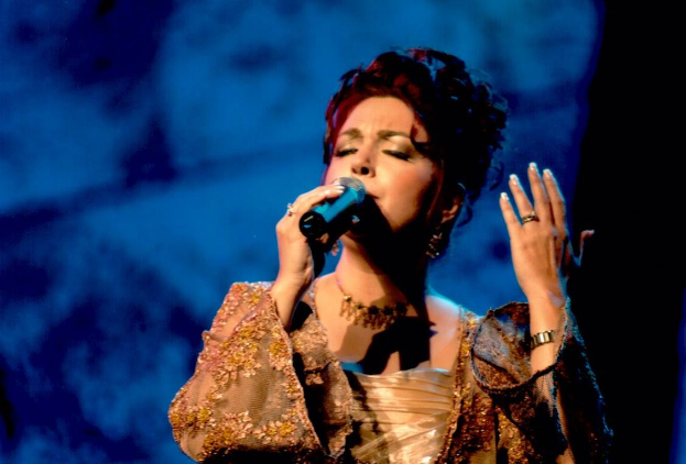 Eine Frau in einem goldenen Kleid, die auf der Bühne der Eurovision Song Contest in ein Mikrofon singt, mit einem blauen und schwarzen Hintergrund.