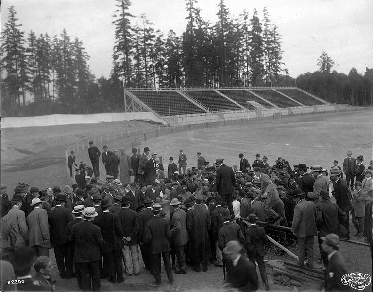 Schwarzes und weißes Foto einer Menge, die sich um ein Fussballfeld versammelt hat, während der Eröffnungszeremonien der Olympischen Spiele 1904, mit Bäumen und einem klaren Himmel im Hintergrund.