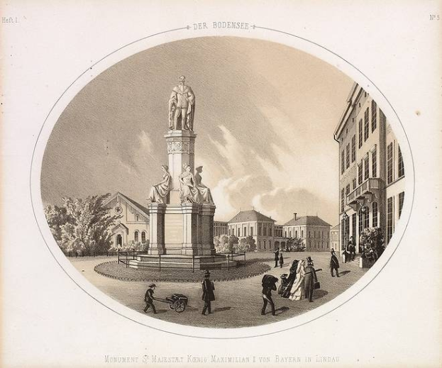 Schwarze und weiße Zeichnung einer Statue des Heiligen Majestrat König Maximilian I. von Bayern in einem Stadtplatz, umgeben von Gebäuden, Bäumen und Menschen, mit Text unten und einem sichtbaren Himmel im Hintergrund.