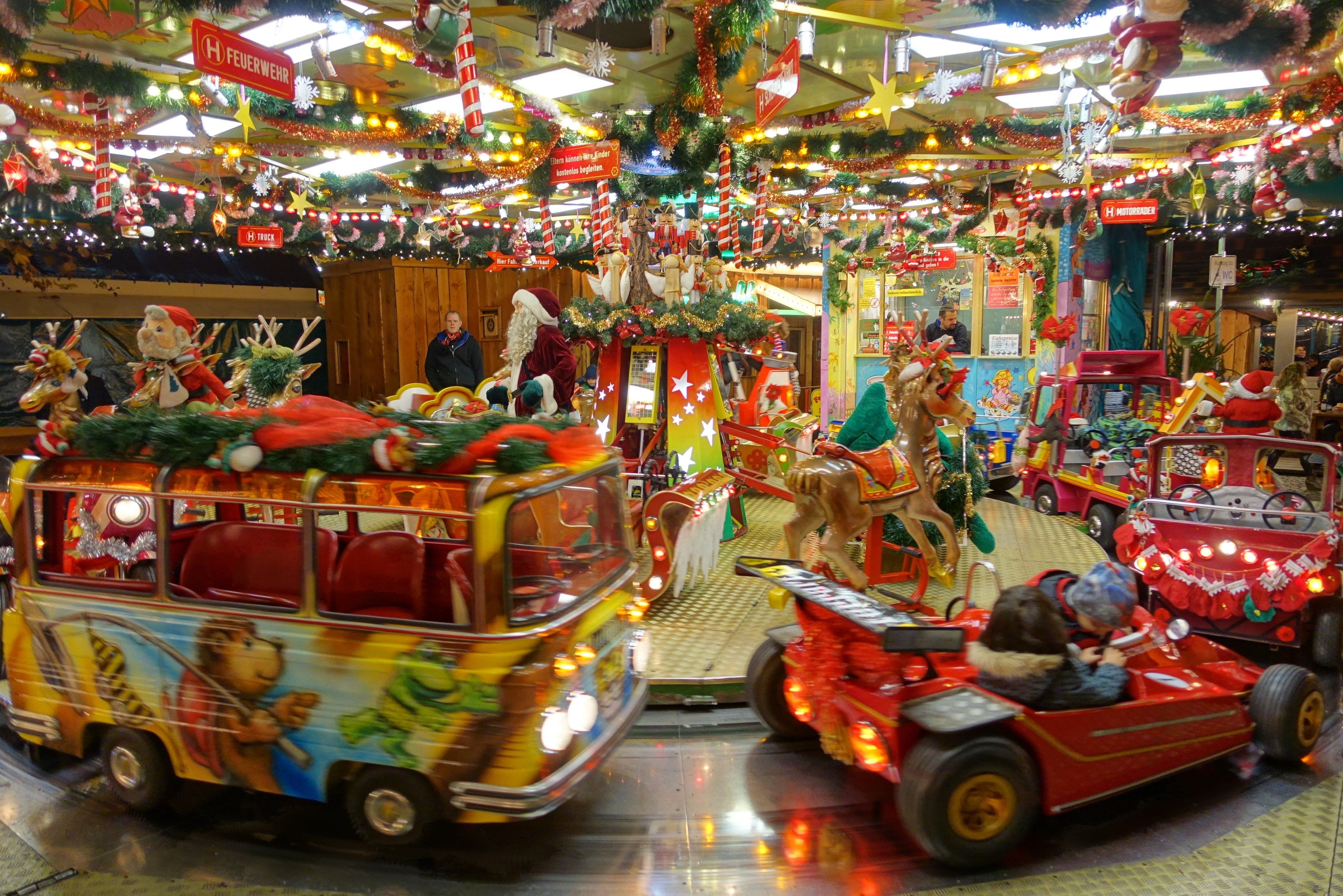 Eine Karussell-Anzeige voller Weihnachtsdekorationen, Spielzeuge, Figuren, Lichter und Texttafeln unter einer Decke mit festlicher Beleuchtung.