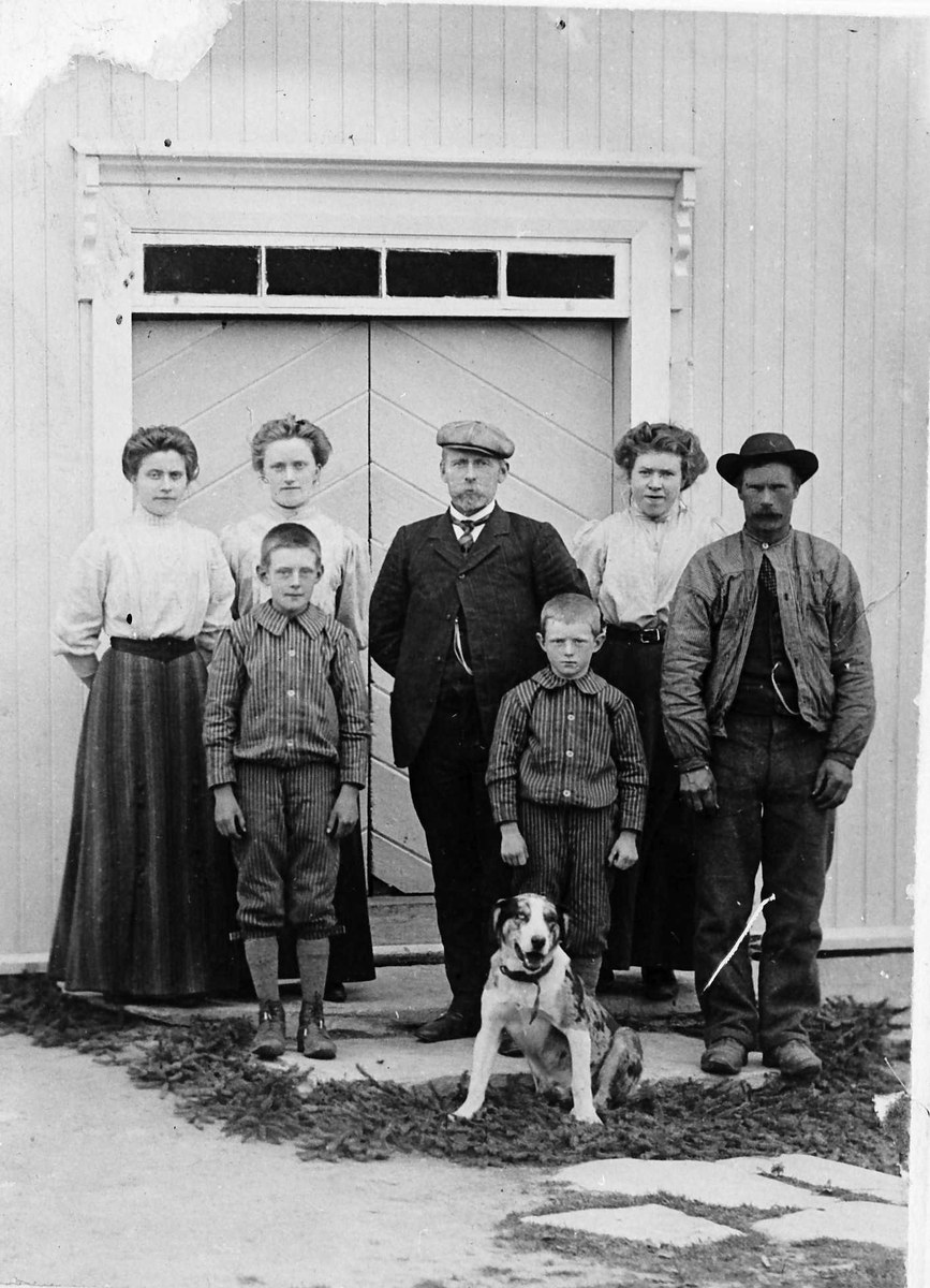 Schwarzes und weißes Foto einer Familie mit einem Hund, die vor einem Haus posieren.